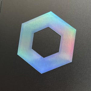 May include: A holographic blue hexagon with a smaller hexagon cut out of the center.