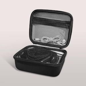 May include: Black, zippered carrying case, open to reveal contents. The case has a mesh pocket in the lid and contains black cables and white cords. The case is designed to protect and organize electronic accessories.