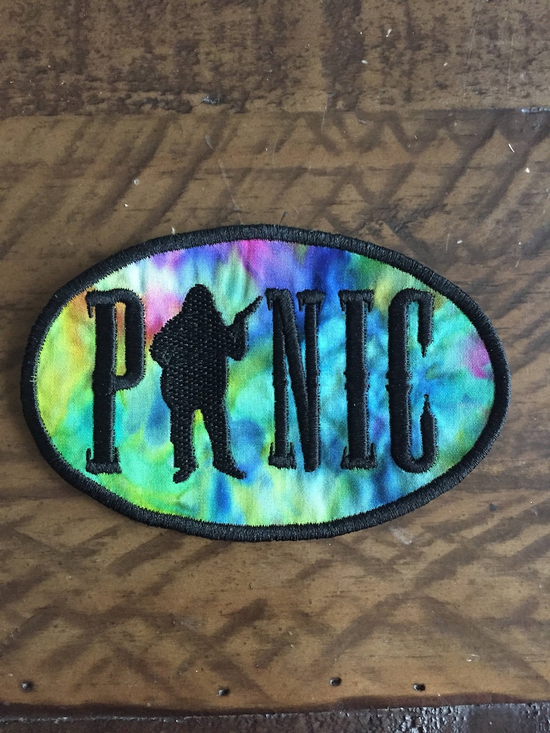 May include: A tie-dye fabric patch with black embroidery of the word "PICNIC" and a silhouette of a person holding a guitar.