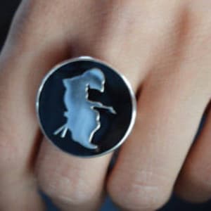 May include: A silver ring with a black enamel design of a person in a crouching pose.