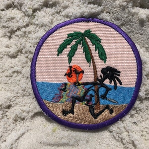 May include: A round embroidered patch with a purple border. The patch features a cartoon stick figure with a palm tree and a setting sun in the background. The stick figure is wearing a colorful patterned shirt and shorts.