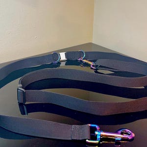 以下が含まれることがあります： 虹色に輝く金属製金具を備えた黒いナイロン製ドッグリード。回転式スナップフック、Dリング、中央のバックルが付いています。リードには長さを調節するためのスライド式パーツが含まれています。