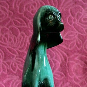 Könnte beinhalten: Eine grüne und schwarze glasierte Keramikfigur eines sitzenden Hundes mit geneigtem Kopf. Der Hund hat eine lange Schnauze und schlaffe Ohren.