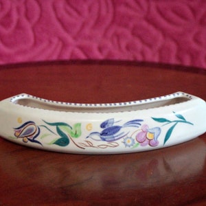 Puede incluir: Un macetero de cerámica blanca con un pájaro azul y un diseño floral. El macetero tiene forma de semicírculo y tiene un pequeño borde alrededor de la parte superior.