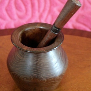 May include: A dark brown wooden mortar and pestle. The mortar is round and has a wide opening. The pestle is long and slender.