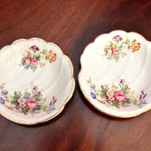 Peut inclure: Deux plats en céramique blanche en forme de coquille avec des bordures dorées et des motifs floraux dans des tons de rose, rouge, bleu et vert.