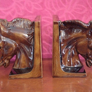 May include: A pair of brown ceramic horse head bookends. The horse heads are facing to the left and right, and the bookends are on a wooden surface.