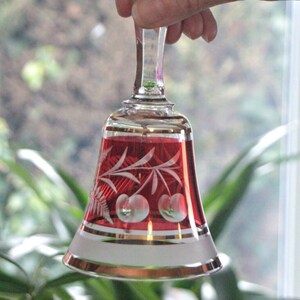 Puede incluir: Una campana de cristal roja con un borde blanco esmerilado y un diseño de cerezas y hojas grabadas. La campana está sostenida por una mano.