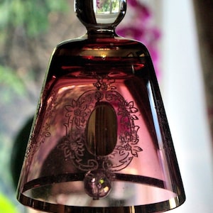Pode incluir: Um sino de vidro vintage com uma tonalidade rosa e intrincados desenhos florais gravados. O sino tem um topo de vidro transparente e uma borda dourada.