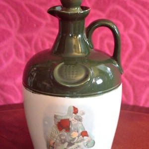 Może przedstawiać: Ceramiczny dzban z ciemnozielonym wierzchem i białą podstawą. Dzbanek posiada uchwyt i wylew. Podstawa ma namalowaną scenę z ludźmi. Dzbanek prawdopodobnie służy do przechowywania płynów.