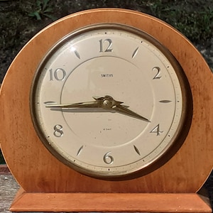 Puede incluir: Un reloj de madera vintage con una esfera de latón y agujas doradas. La esfera del reloj dice "Smiths 8 Day".