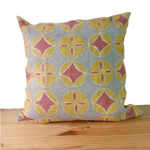 May include: A grey throw pillow with a geometric pattern of red and yellow diamonds and circles. The pillow is made of a linen fabric and has a slightly textured surface.
