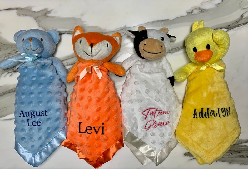Peut inclure: Quatre couvertures pour b&eacute;b&eacute; en peluche avec des attaches de t&ecirc;te d'animaux. Les couvertures sont bleues, orange, blanches et jaunes. Les animaux sont un ours, un renard, une vache et un canard. Les couvertures sont personnalis&eacute;es avec les noms : August Lee, Levi, Tatum Grace et Addalyn.