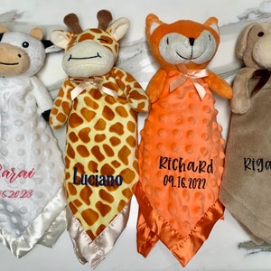 Peut inclure: Quatre couvertures pour b&eacute;b&eacute; en peluche avec des animaux et des noms brod&eacute;s ainsi que des dates. Les couvertures sont blanches, brunes, orange et beige. Les animaux sont une vache, une girafe, un renard et un chien.