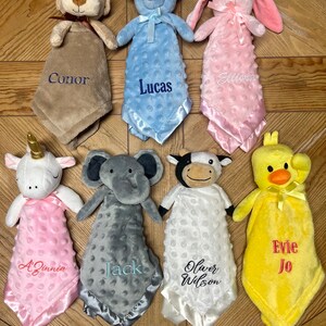 Peut inclure: Sept peluches avec des couvertures personnalis&eacute;es. Les peluches comprennent un chien, un ours, un lapin, une licorne, un &eacute;l&eacute;phant, une vache et un poussin. Les couvertures sont de diff&eacute;rentes couleurs, notamment le marron, le bleu, le rose, le blanc, le gris et le jaune. Chaque couverture porte un nom brod&eacute;, notamment Conor, Lucas, Eliana, A'Zinnia, Jack, Oliver Wilson et Evie Jo.