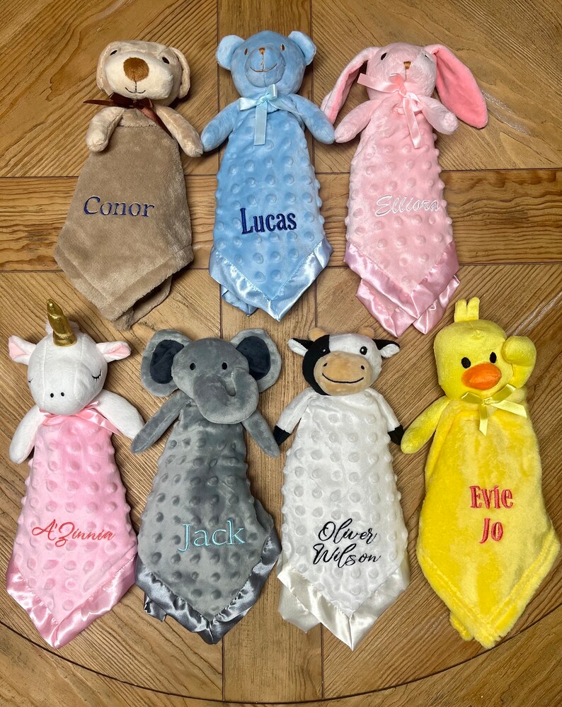 Peut inclure: Sept peluches avec des couvertures personnalis&eacute;es. Les peluches comprennent un chien, un ours, un lapin, une licorne, un &eacute;l&eacute;phant, une vache et un poussin. Les couvertures sont de diff&eacute;rentes couleurs, notamment le marron, le bleu, le rose, le blanc, le gris et le jaune. Chaque couverture porte un nom brod&eacute;, notamment Conor, Lucas, Eliana, A'Zinnia, Jack, Oliver Wilson et Evie Jo.