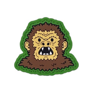 May include: Green and brown embroidered patch with a cartoon image of a bigfoot's face with a menacing expression.