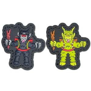 May include: Two black and white embroidered patches featuring a cartoon creature with horns, a red belt, and a stick. One creature is black and the other is green.