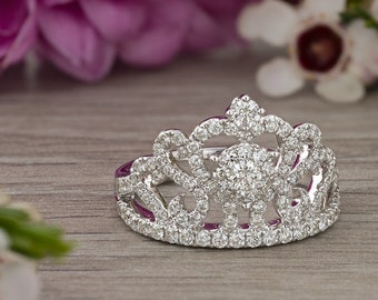 May include: A silver tiara ring with a row of clear cubic zirconia stones. The ring is surrounded by white and pink flowers.