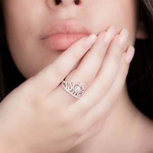 May include: A silver ring with a crown design set with clear cubic zirconia stones.