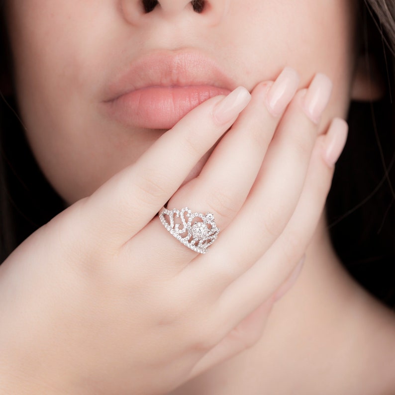 May include: A silver ring with a crown design set with clear cubic zirconia stones.