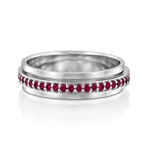 May include: A silver band with a row of small, red gemstones around the edge.