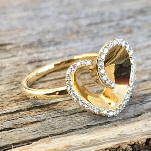 May include: A gold ring with a heart-shaped design. The heart is outlined with small, clear stones.
