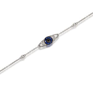 Könnte beinhalten: Ein silbernes Kettenarmband mit einem blauen und schwarzen bösen Augen-Anhänger. Der Anhänger ist von kleineren weißen und schwarzen Steinen umgeben.