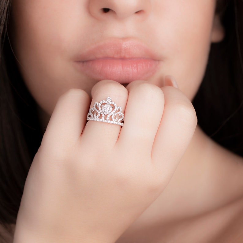 May include: A silver ring with a crown design set with clear cubic zirconia stones.