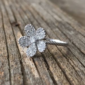 May include: A silver ring with a flower design set with clear cubic zirconia stones.