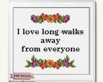 May include: Cross-stitch pattern framed in white, featuring the text "I love long walks away from everyone." Floral accents in red, yellow, and purple adorn the top and bottom. The words "PDF Pattern" and "DeLoraiPatterns" are also visible.