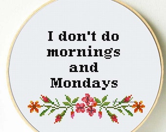 May include: A white embroidery hoop with a black and white cross-stitch design that reads "I don't do mornings and Mondays". The design is surrounded by a floral border with pink and orange flowers.