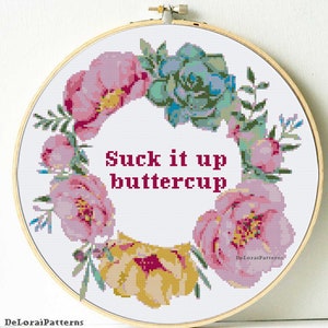 May include: Cross stitch pattern featuring a floral wreath with pink, yellow, and green flowers. The text "Suck it up buttercup" is in the center of the wreath.