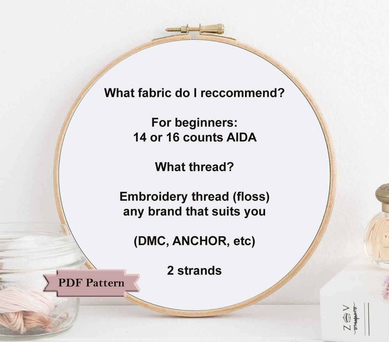 May include: A close-up of a wooden embroidery hoop with instructions for beginners on what fabric and thread to use for embroidery. The text reads: "What fabric do I recommend? For beginners: 14 or 16 counts AIDA. What thread? Embroidery thread (floss) any brand that suits you (DMC, ANCHOR, etc) 2 strands. PDF Pattern."