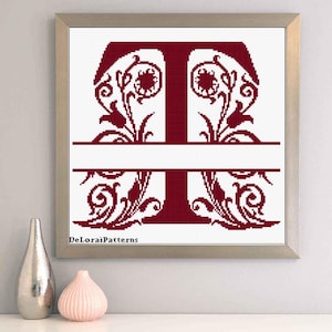 May include: Framed cross-stitch art featuring a claret letter "T" with floral embellishments. The letter is divided by a horizontal white space. The artwork is in a silver frame. The text "DeLoraiPatterns" is visible.