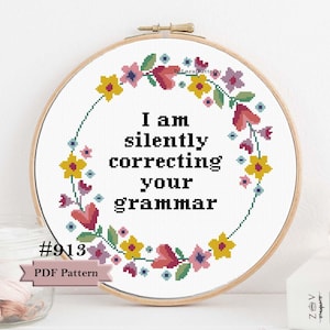 Puede incluir: Un bastidor de bordado de punto de cruz con el texto "I am silently correcting your grammar" rodeado por una corona floral. El bastidor es de madera y presenta una etiqueta de patrón PDF con el número #913.