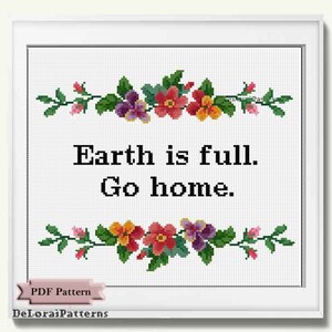 May include: Framed cross-stitch art with the text "Earth is full. Go home." The artwork features floral borders in red, orange, purple, and pink. The frame is white, and the background is a grid pattern.
