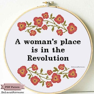 May include: A white cross-stitch pattern with a floral border and the text "A woman's place is in the Revolution".