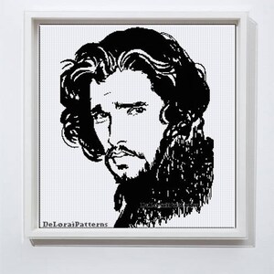 May include: A framed cross-stitch portrait in black and white, depicting a man with long, wavy hair and a mustache. The artwork is a detailed face, set in a white frame. The artist's name, DeLoraiPatterns, is visible in the lower left corner.