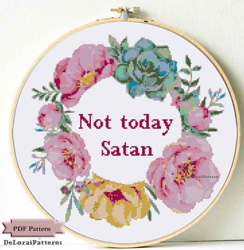 Może przedstawiać: Biały tamborek do haftu z wzorem wieńca kwiatowego i tekstem "Not today Satan" w kolorze czerwonym. Wieniec wykonany jest z r&oacute;żowych i ż&oacute;łtych kwiat&oacute;w oraz zielonych liści.