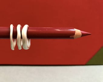May include: Three silver rings stacked on top of each other, resting on a red pencil.