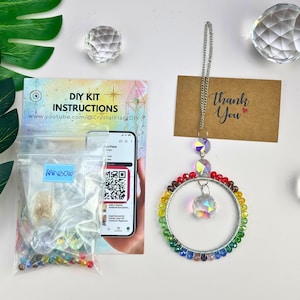 May include: A DIY kit with instructions, a rainbow-colored crystal suncatcher, and a thank you card. The suncatcher features a rainbow-colored beaded circle with a crystal pendant. Additional crystal spheres are also present.