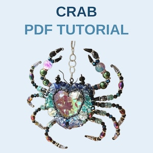May include: A beaded crab ornament featuring a large central heart-shaped iridescent crystal surrounded by blue, green, and black beads. The crab has eight legs and two claws made of wire and beads, with a silver chain attached. Text reads CRAB PDF TUTORIAL.