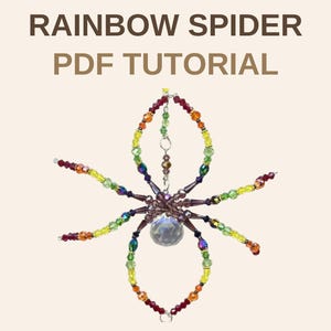 Puede incluir: Un adorno de araña hecho con cuentas que presenta una esfera central de cristal transparente facetado y ocho patas construidas con cuentas de vidrio multicolor en rojo, naranja, amarillo, verde y morado. El texto RAINBOW SPIDER PDF TUTORIAL aparece arriba.