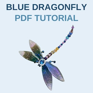 May include: A dragonfly ornament featuring iridescent blue and purple wings with a central oval blue stone surrounded by small clear crystals. The long tail is composed of a series of multi-colored beads. The text BLUE DRAGONFLY PDF TUTORIAL is visible.