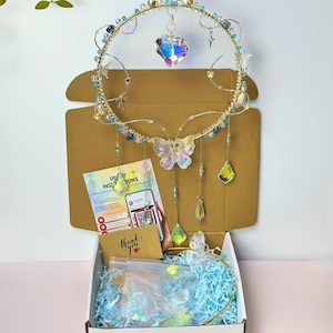 May include: A handmade headpiece with a gold wire frame, decorated with iridescent crystals, beads, and a butterfly. The headpiece is presented in an open cardboard box with blue filler and a "thank you" card.