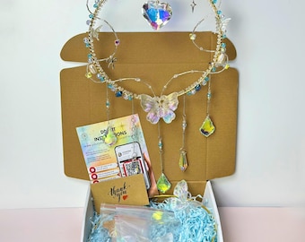 May include: A celestial-themed, handmade headpiece with a gold wire frame, adorned with iridescent crystals, beads, and a butterfly centerpiece. The headpiece is displayed in an open cardboard box with blue filler and a "thank you" card.