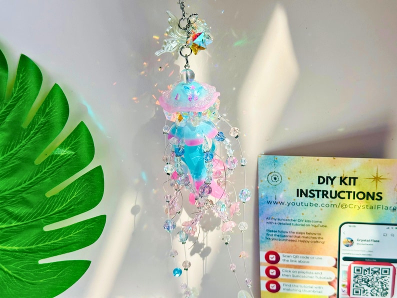 May include: A hanging jellyfish suncatcher with a blue, pink, and clear beaded design. The suncatcher has a jellyfish shape with a pink and blue top and a clear beaded body. A DIY kit instruction card is visible.