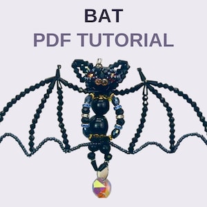 Puede incluir: Una figura de murciélago hecha de cuentas negras facetadas, con alas anchas, un cuerpo redondo y un colgante de cristal iridiscente. El texto BAT PDF TUTORIAL aparece en letras gris oscuro sobre el adorno de cuentas.