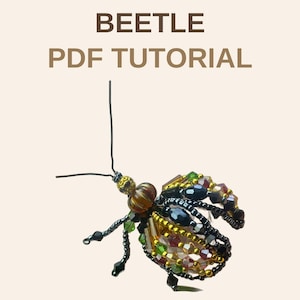 May include: A beaded beetle ornament crafted from black, gold, green, and amber-colored crystals and seed beads. The insect features two thin wire antennae and text above that reads BEETLE PDF TUTORIAL in brown capital letters.